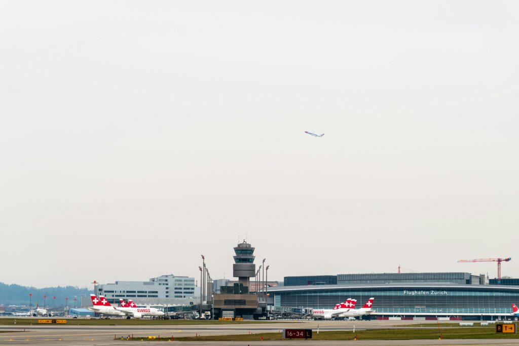 pexels-photo-17166884-17166884 Swiss airplanes at Zurich Airport with control tower and terminal in background.